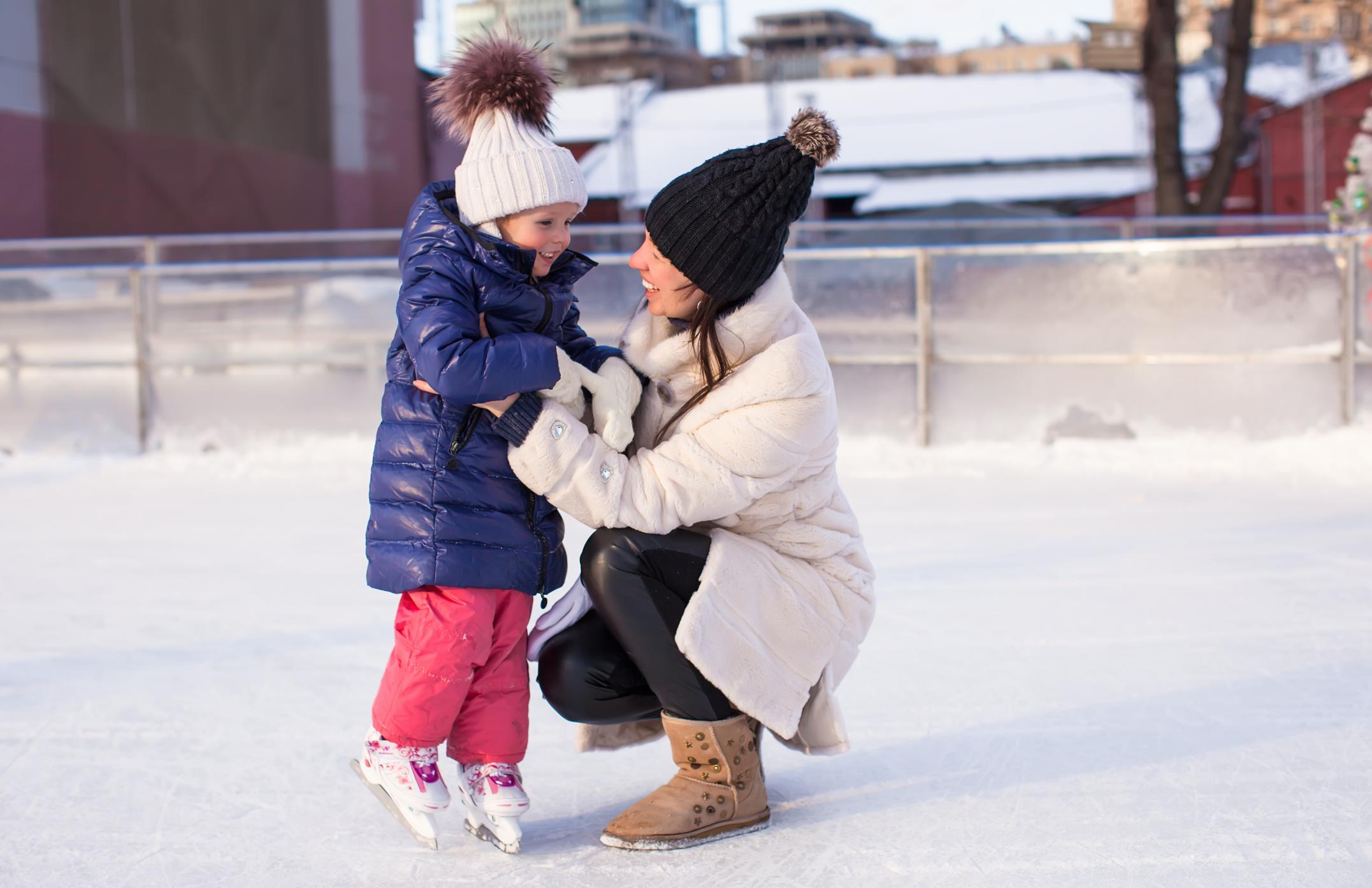 young-mother-teaching-her-little-daughter-to-skate-on-ice-rink