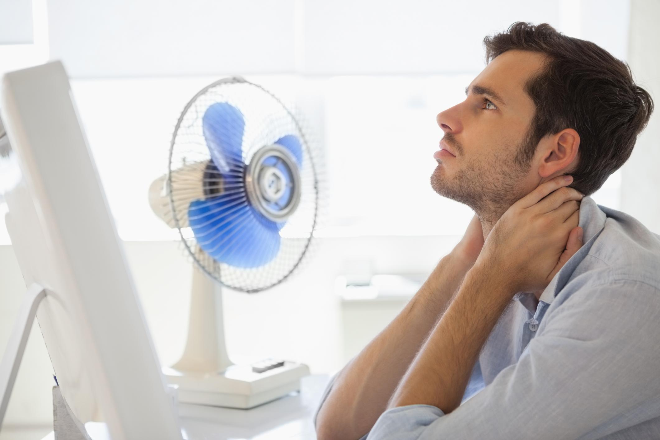 Man with computer and fan cooling off